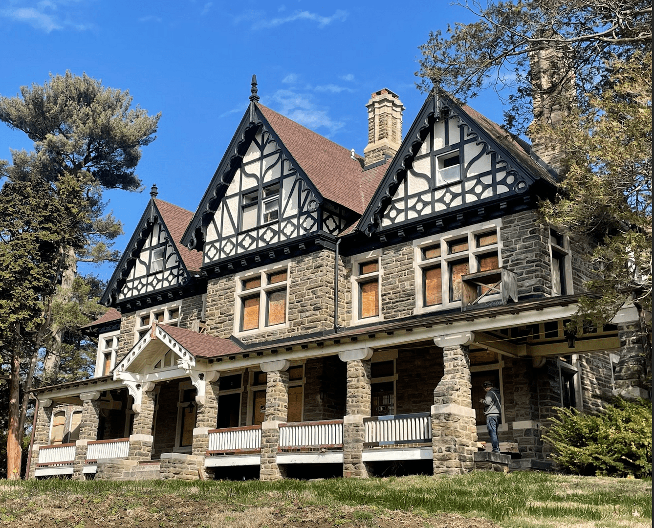 Elegant Tudor Revival house with a stone-columned covered porch and three peaked roofs.