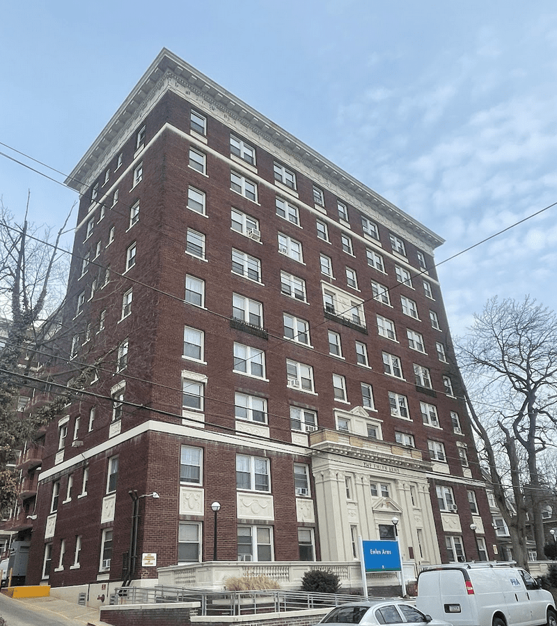 Nine-story red brick NeoClassical apartment building with a large stone surround at the entryway and a dentil cornice.